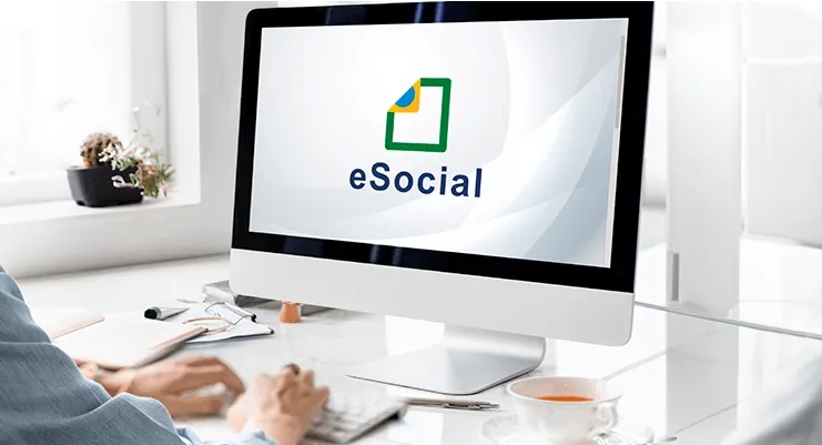Pessoa digitando em um computador de mesa com o logotipo do eSocial na tela, em um escritório claro