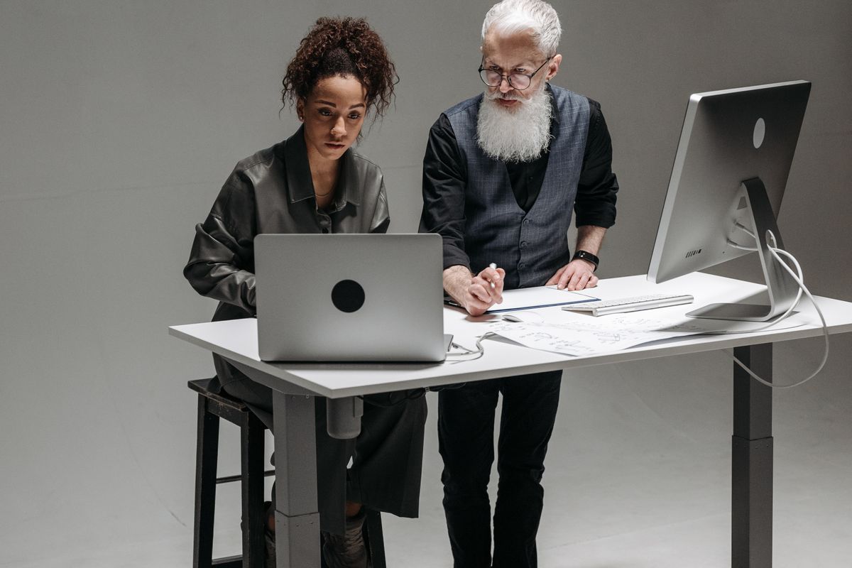Duas pessoas trabalhando em uma mesa de altura regulável com computador