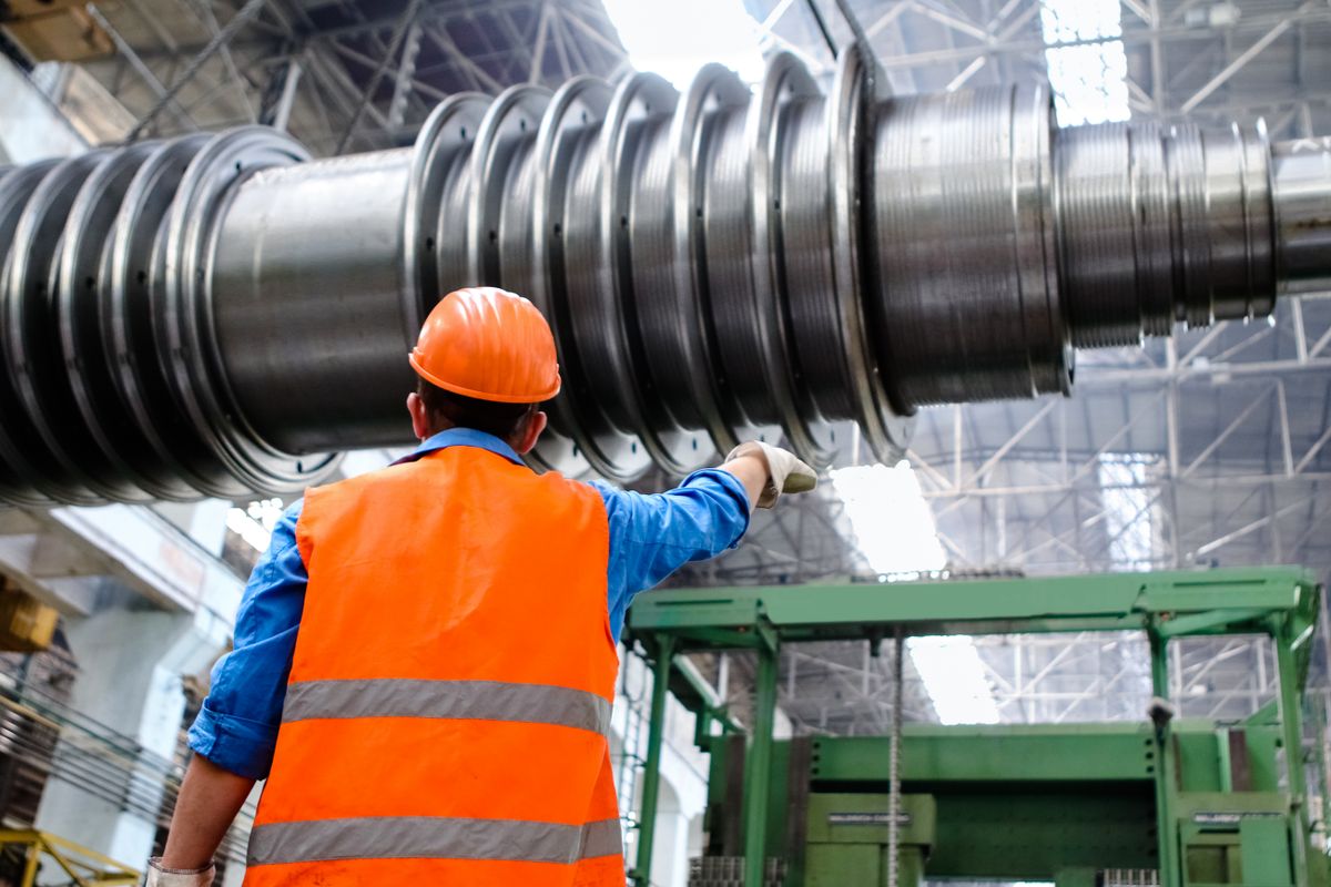 Trabalhador de capacete e colete refletivo inspecionando máquinas em uma indústria