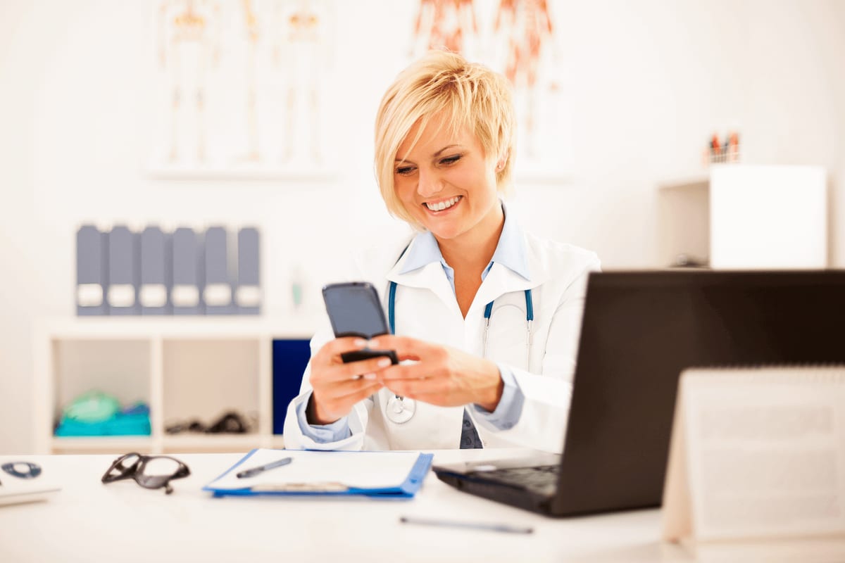 Médica do trabalho usando o celular e o computador em seu consultório